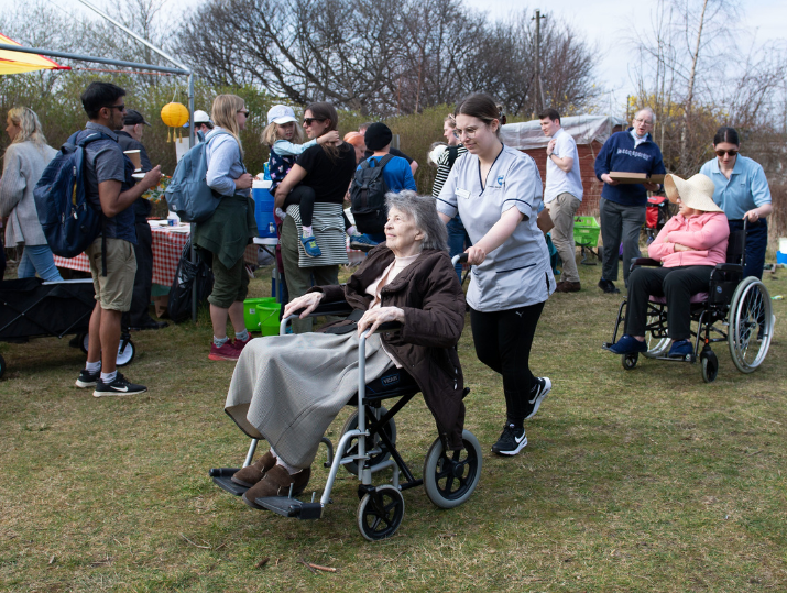 Two wheelchair users are assisted by support workers past a crowd at the PCHP event.