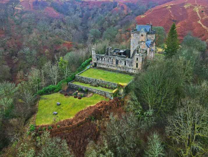 The ruins of Castle Campbell nestled in stepped gardens against a backdrop of hills and woodland.