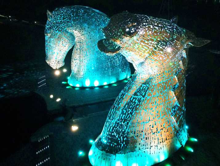 An aerial photograph showing the huge metal sculptures of the Kelpies at Falkirk, lit up at night.